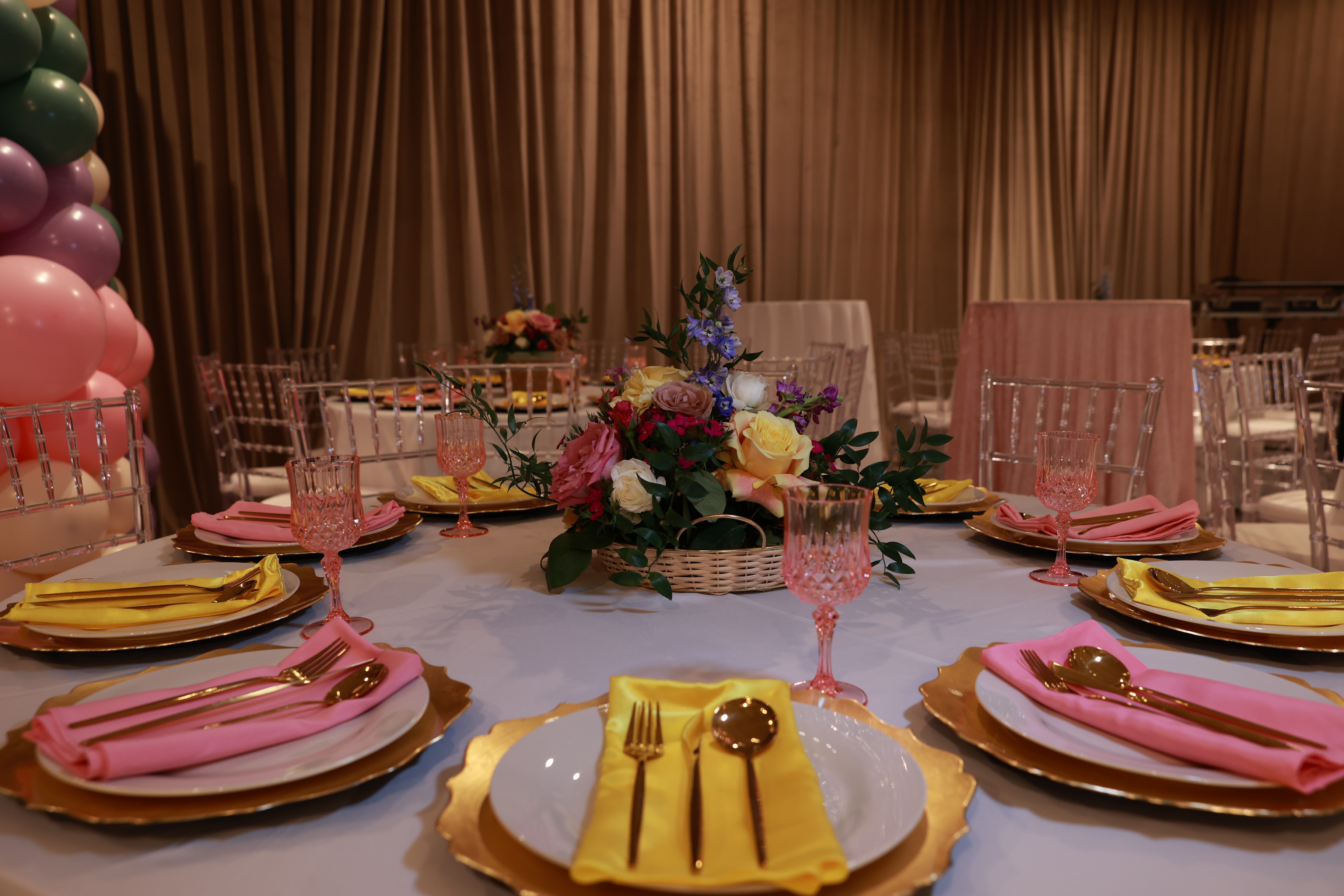 Pink and yellow tablescape with florals, gold flatware, and crystal chairs