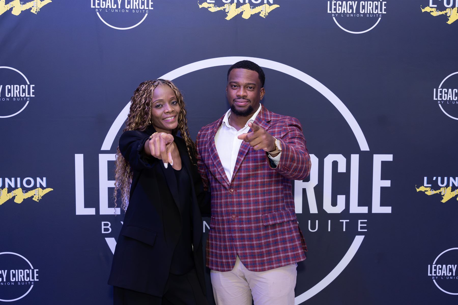 Two guests pointing at the camera in front of the Legacy Circle step-and-repeat